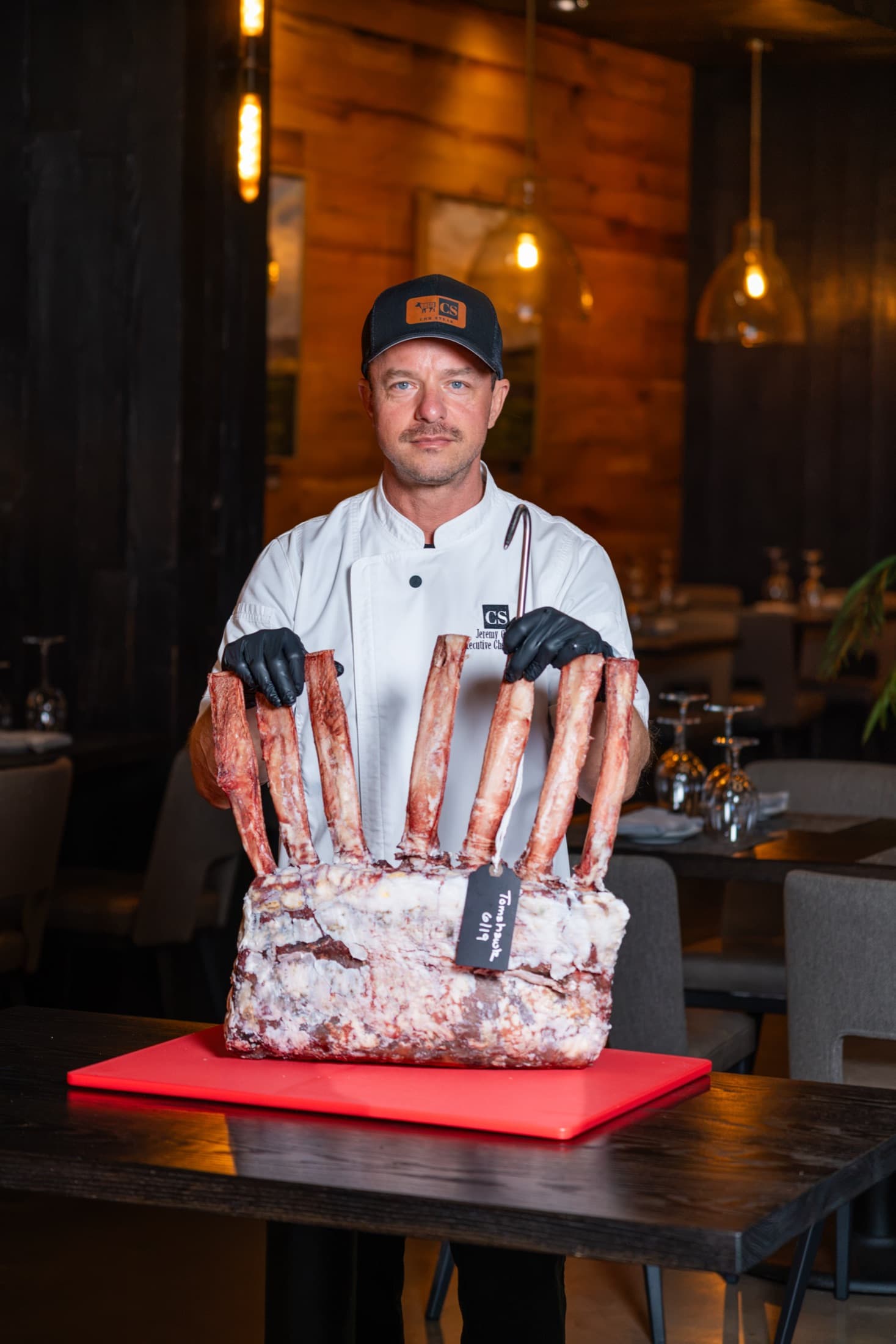 Executive chef and owner Jeremy Green holding a whole dry-aged tomahawk rib rack with a handwritten tag