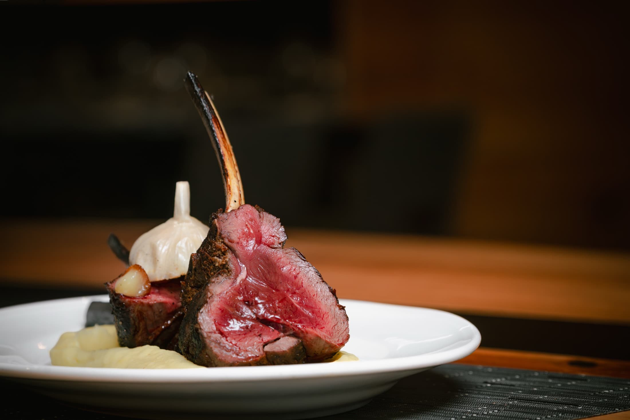 An elk rack chop sliced to show a medium rare center, served over puree at CHR Steak in Gainesville, Georgia