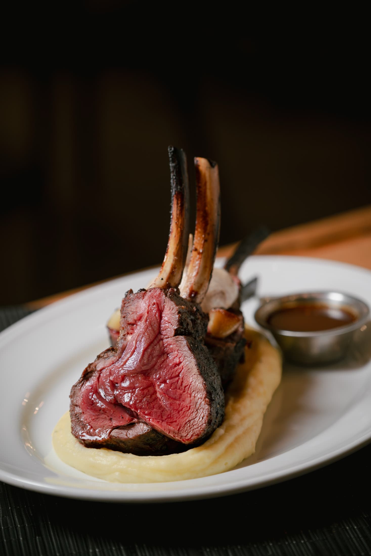 Frenched bones standing tall on a game rack served with a ramekin of sauce at CHR Steak