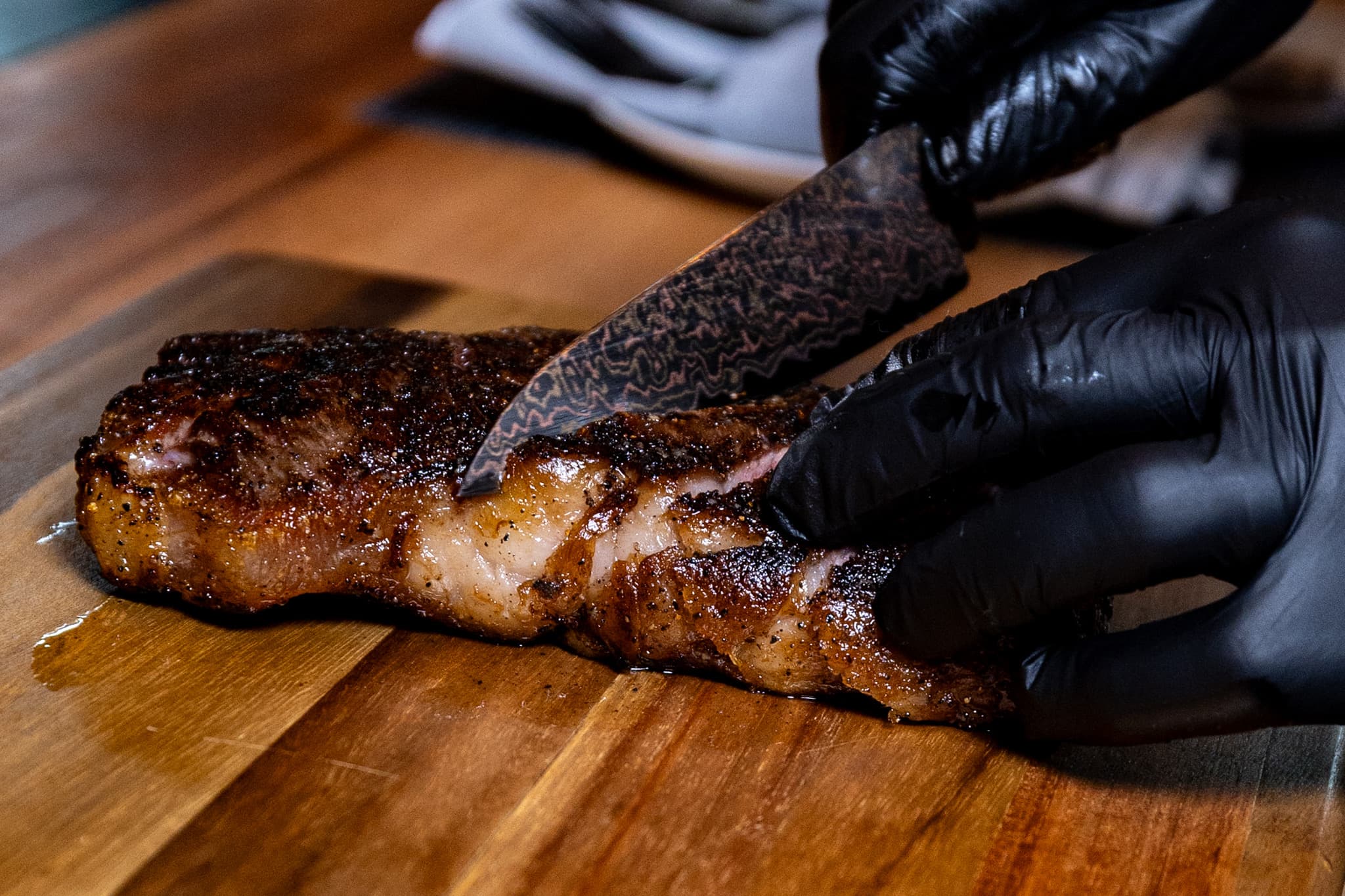 A seared strip steak being sliced on a wooden board at CHR Steak