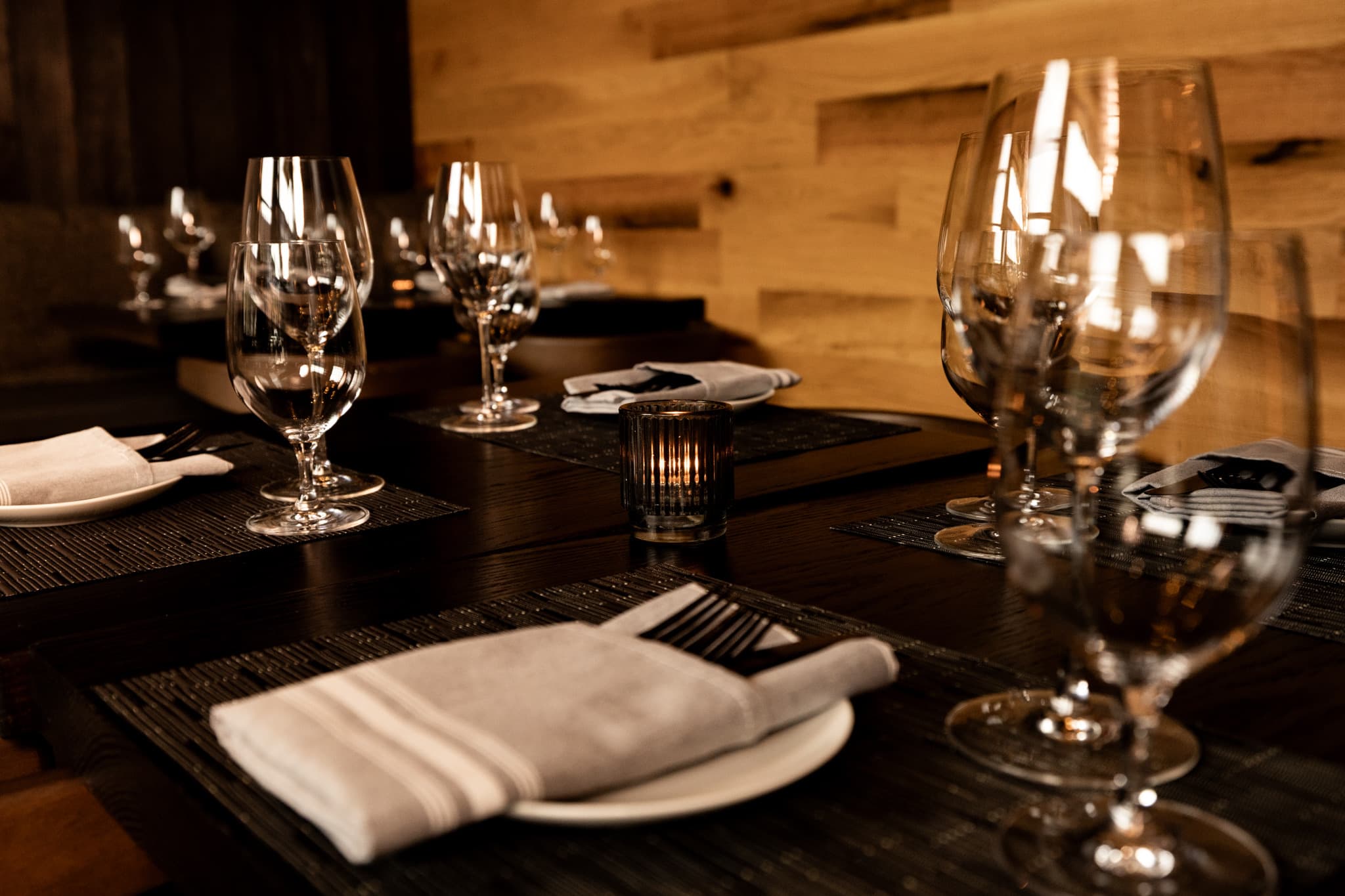 Wine glasses and folded napkins set along a dark table in the private dining room at CHR Steak in Gainesville, Georgia