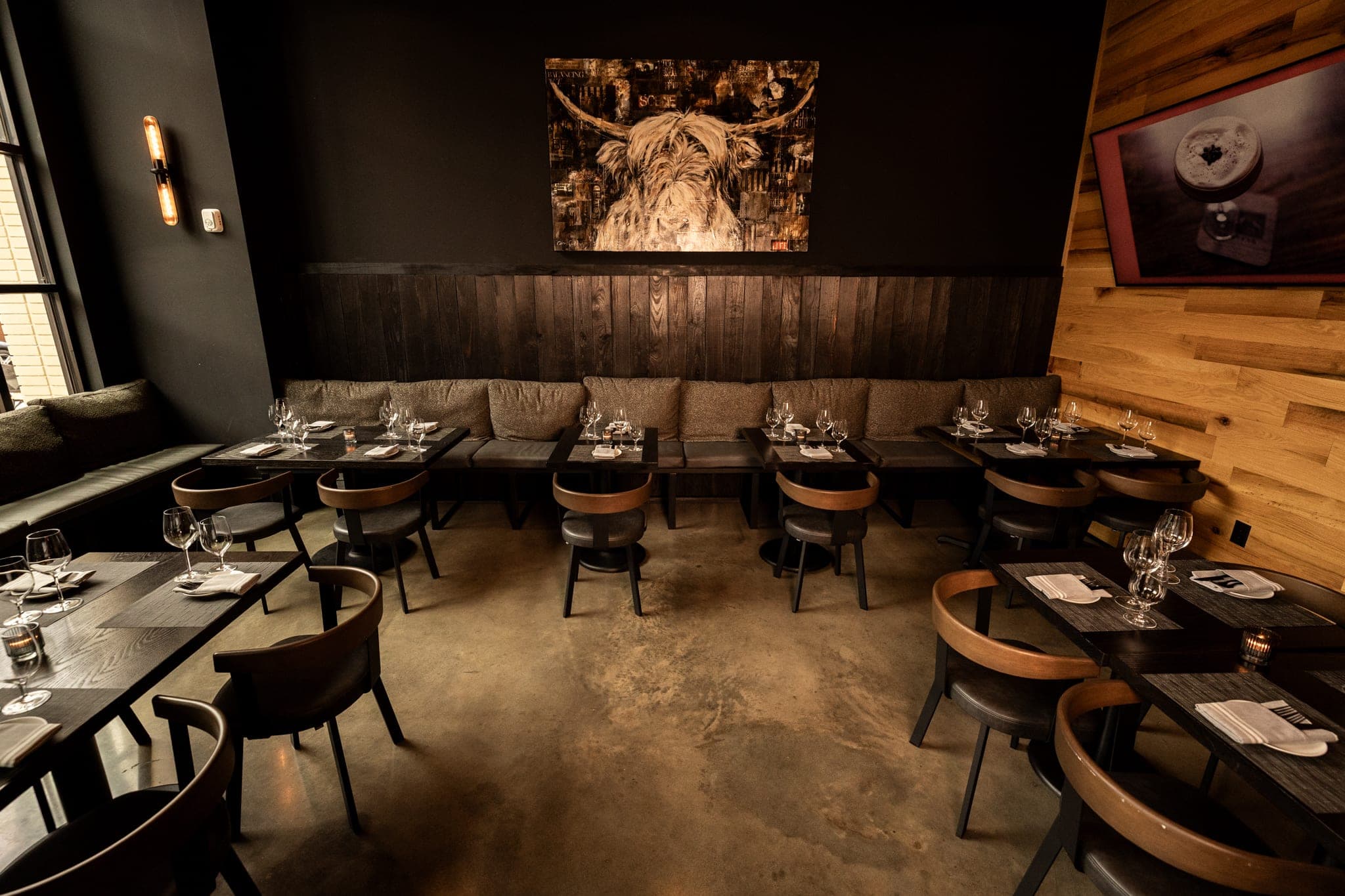 Banquette seating and set tables beneath the highland cow painting in the CHR Steak private dining room