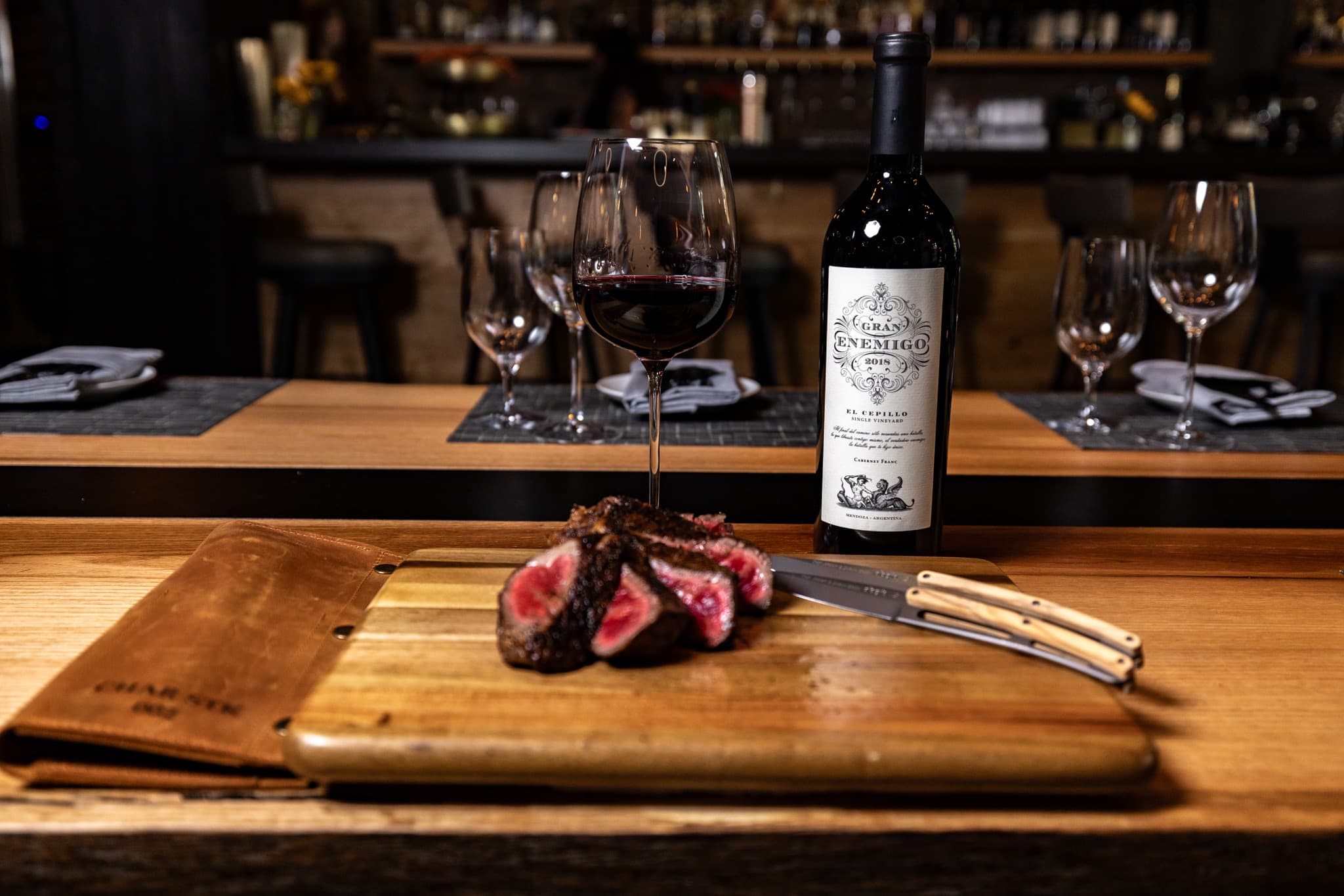 A Blade Club leather knife roll and engraved steak knives on a board beside sliced steak in the dining room at CHR Steak in Gainesville, Georgia