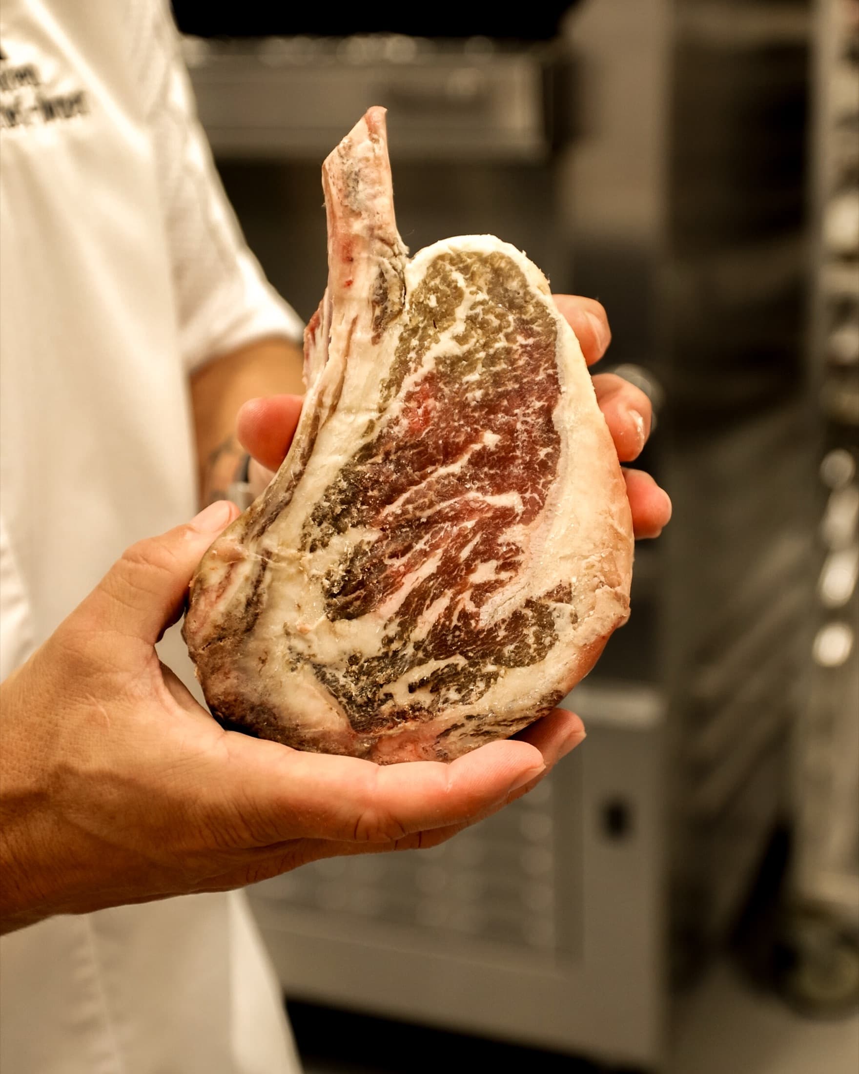 A chef holding a dry-aged bone-in ribeye showing the dark aged crust in the kitchen at CHR Steak in Gainesville, Georgia
