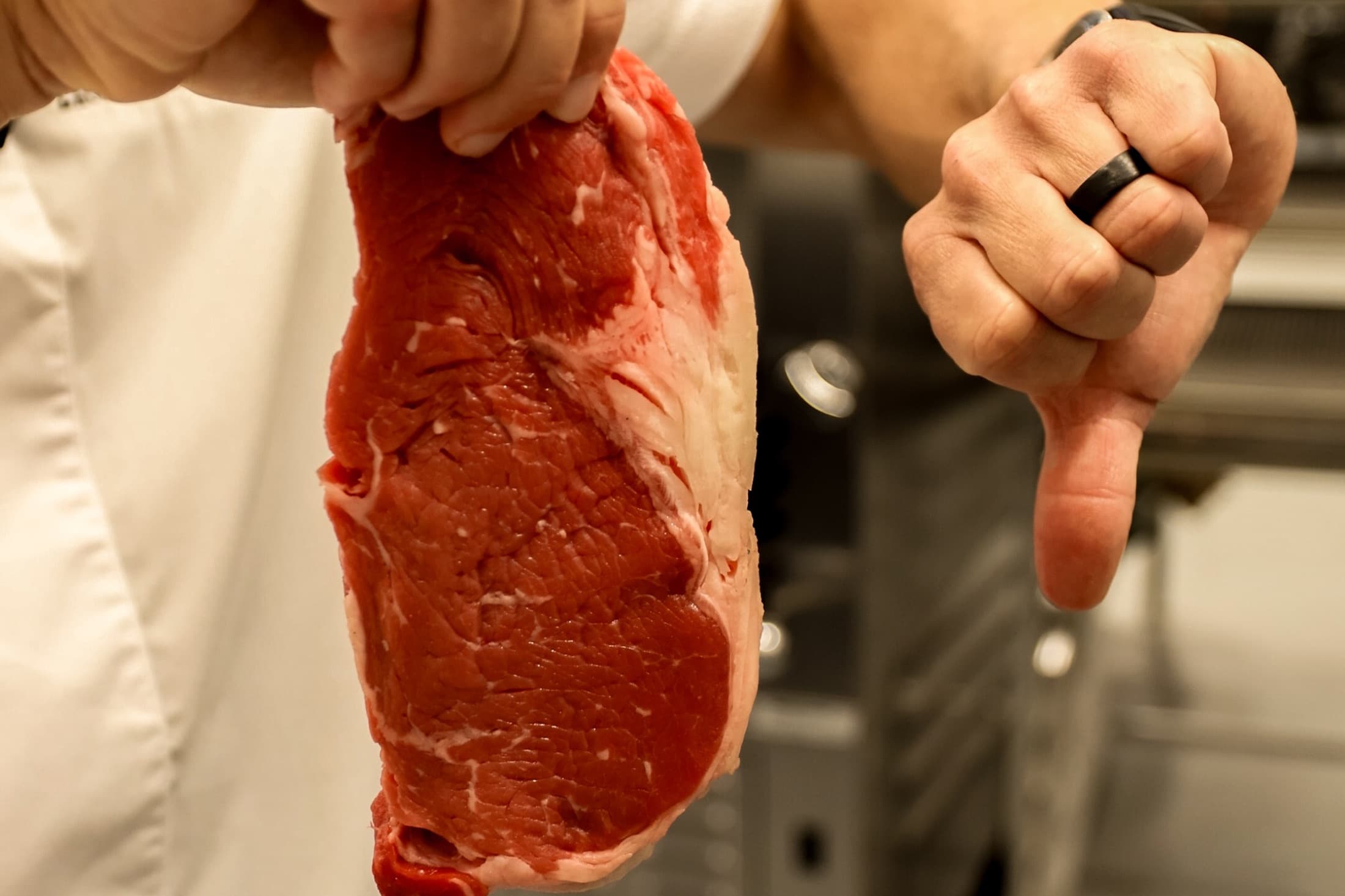 A chef holding up a lean raw steak with very little marbling and giving it a thumbs down in the kitchen at CHR Steak in Gainesville, Georgia