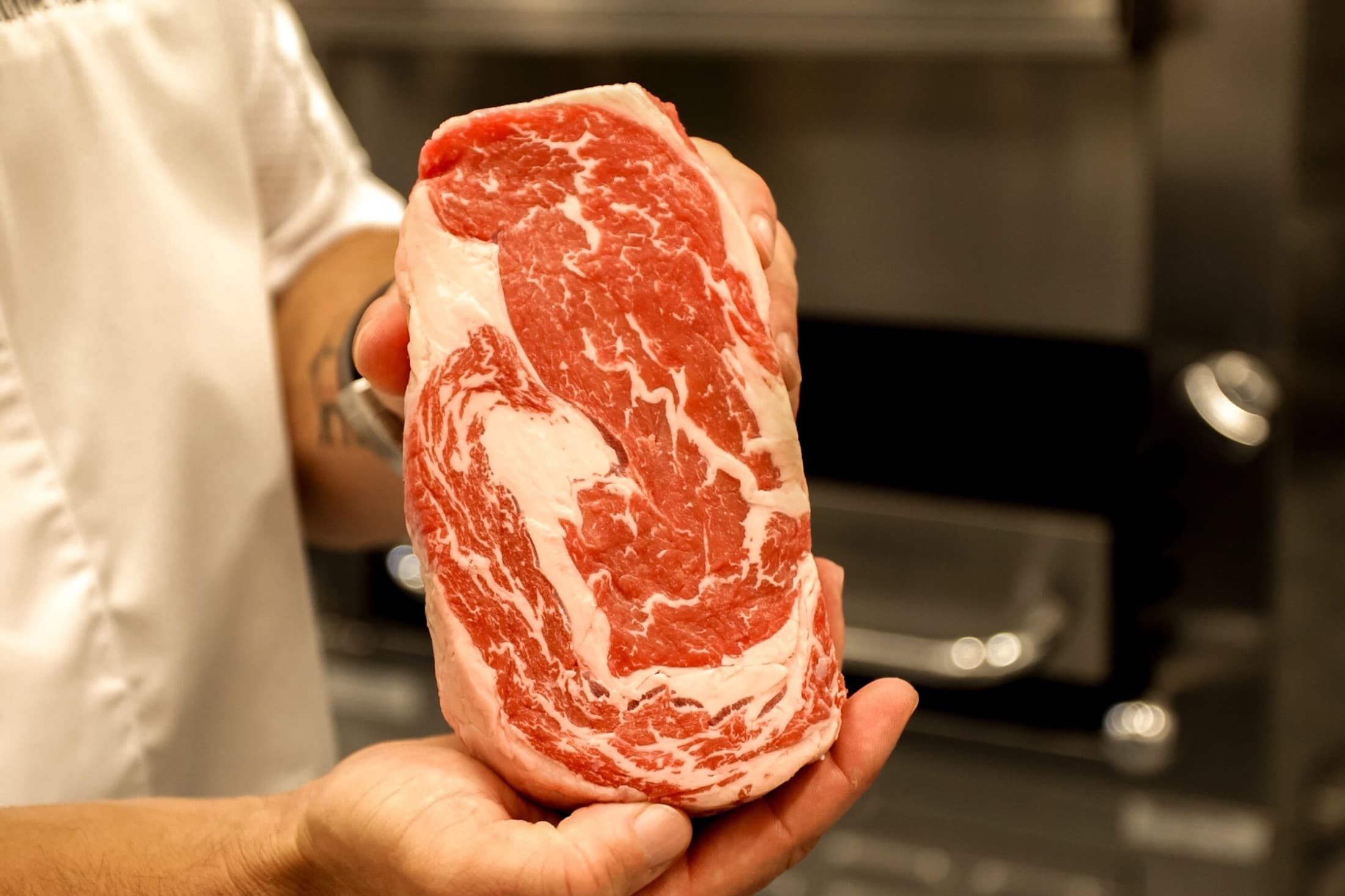 A chef holding a thick raw ribeye with heavy marbling through the whole cut in the kitchen at CHR Steak in Gainesville, Georgia