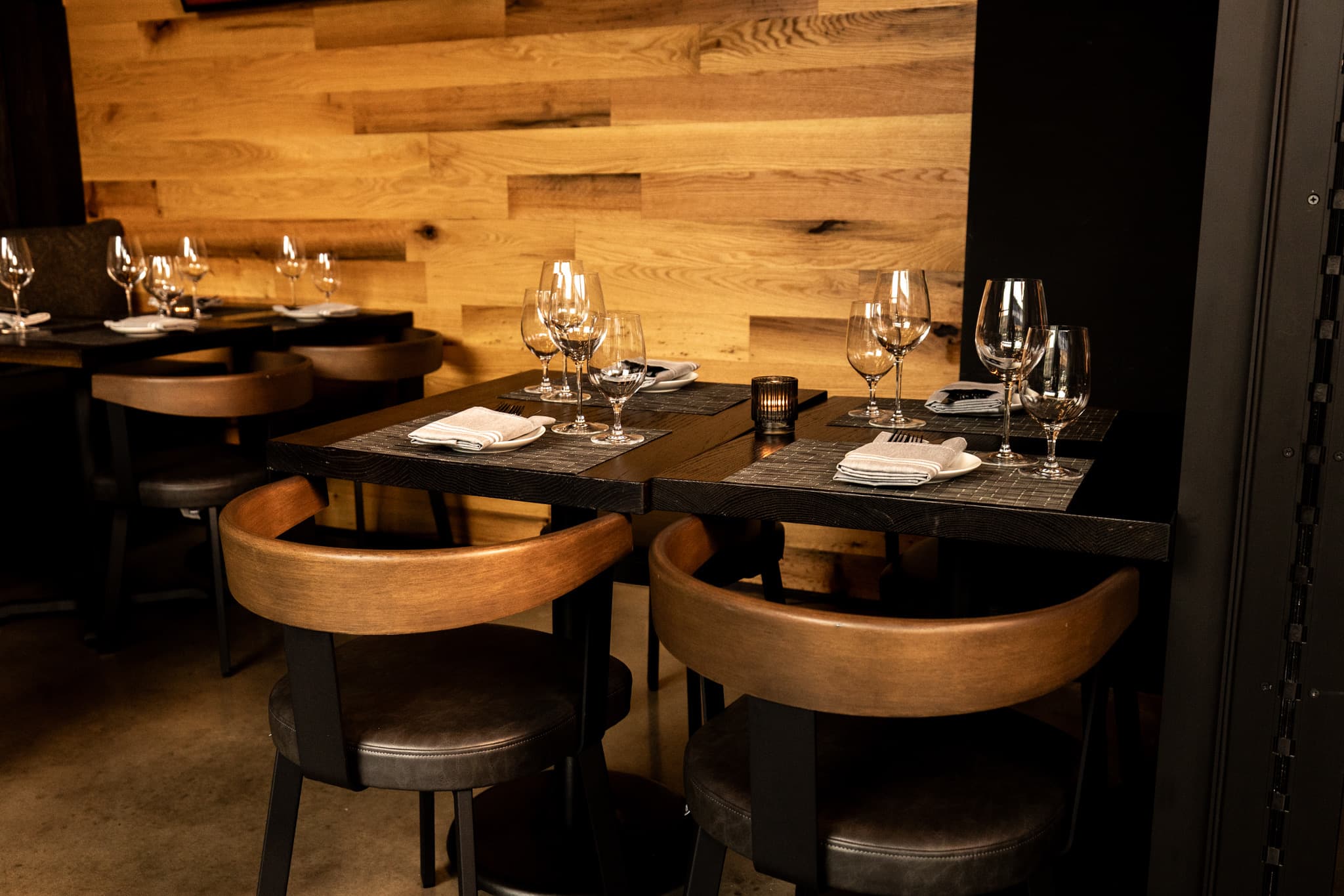 A table set for four with glassware against the wood wall in the dining room at CHR Steak in Gainesville, Georgia